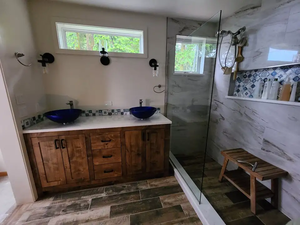 Bathroom with a glass walk-in shower, marble-look wall tile, blue patterned niche and wood-look floor tile, set by a tile contractor in Port Townsend, WA